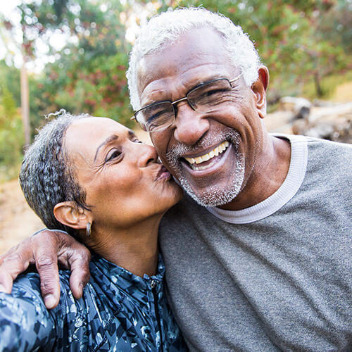 Older woman kissing a man on the cheek while the man is smiling at the camera